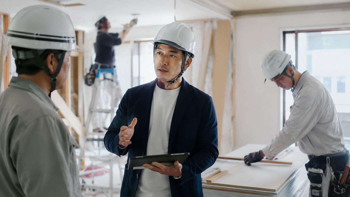 ヘルメットを着けた診断担当者がタブレットを手に、施工中の現場で職人と打ち合わせている様子